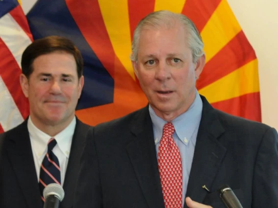 UArizona President Robbins stands at a podium giving remarks as Governor Ducey stands behind him