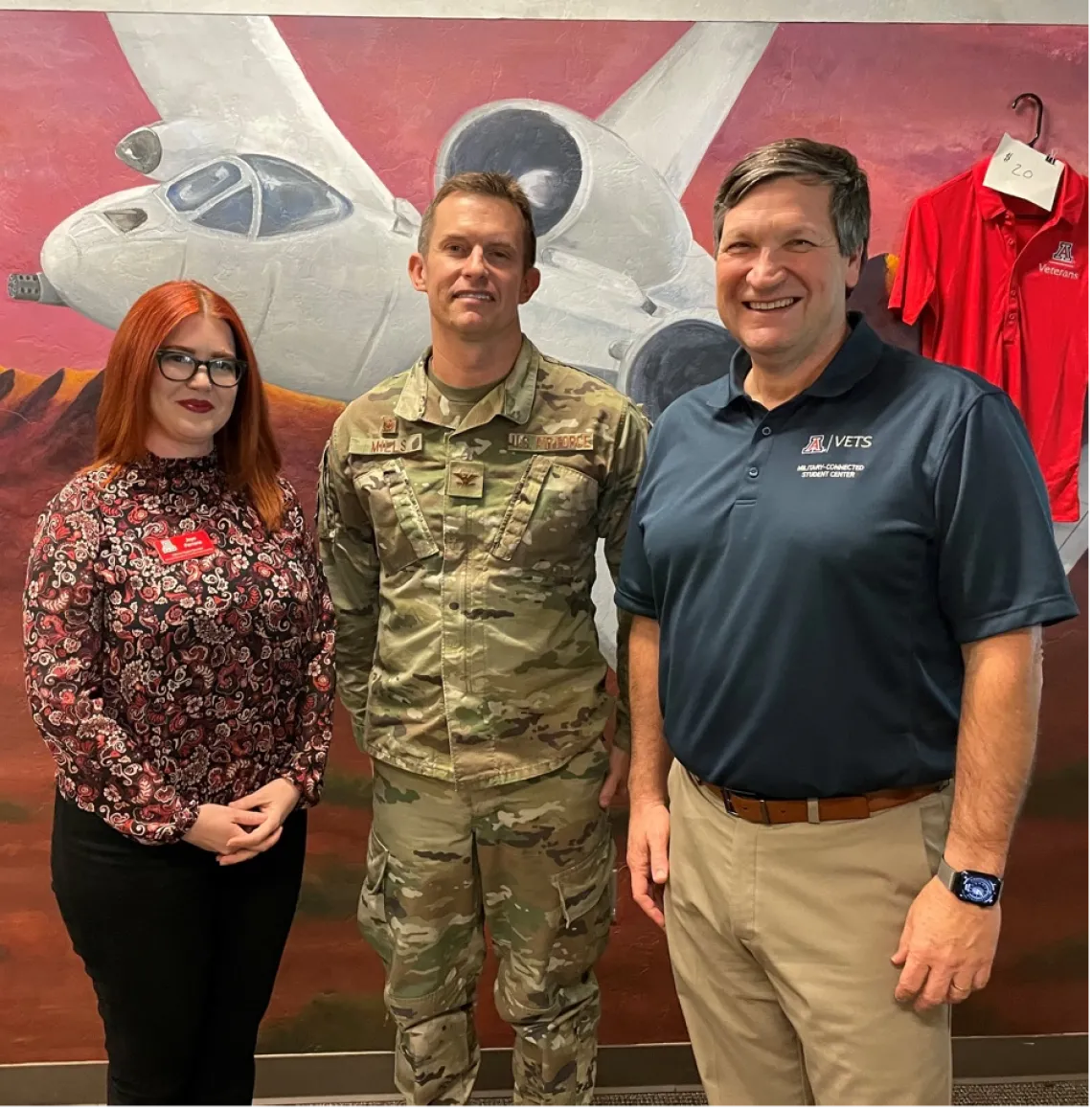 Bruce Grissom, Director of the Veterans Education and Transitions Services program and Jaye Ferrone, our Online Veteran Support Specialist pose for a photo with Colonel Mills in front of an A-10 mural painted by UA vets.