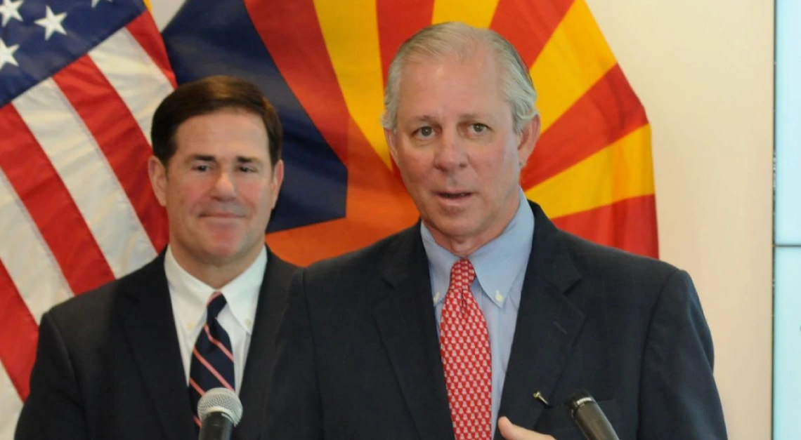 UArizona President Robbins stands at a podium giving remarks as Governor Ducey stands behind him