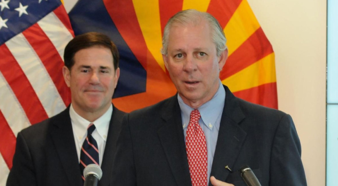 UArizona President Robbins stands at a podium giving remarks as Governor Ducey stands behind him