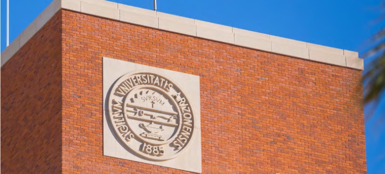 Tight shot of the University of Arizona seal engraved and mounted at the top of the Administration Building which is made of red brick
