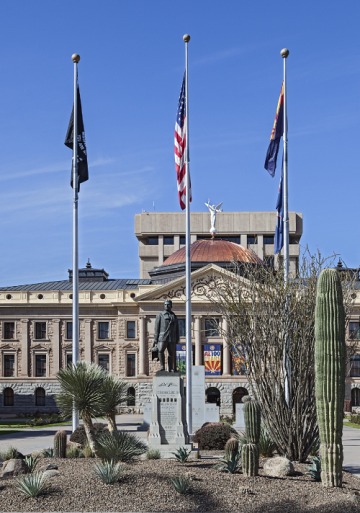 Three flags flying in the foreground in front of the Arizona State Capitol building