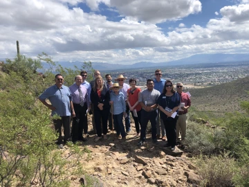 Photo of a group of community leaders and university staff pose for a photo atop the University of Arizona's Tumamoc Hill